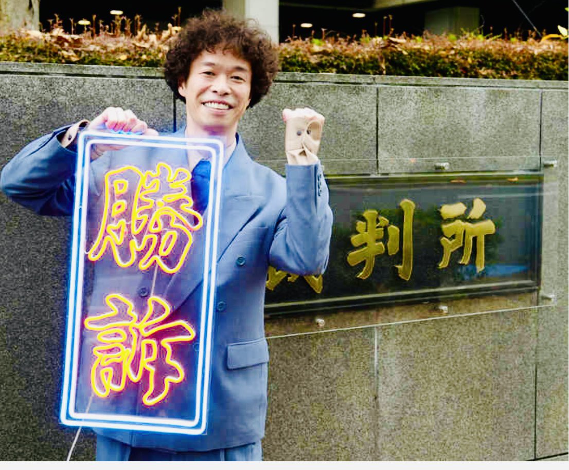 勝訴ボードを掲げる渡邊センス氏